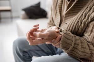 senior man with parkinsonism holding trembling hand while sitting at home